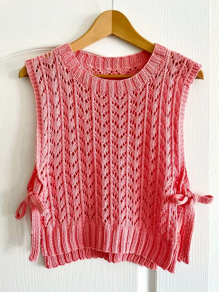 A hand knitting pink lace knit top hanging on a wooden hanger