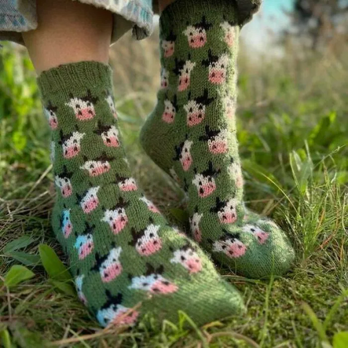 Person wearing green socks decorated with knitted pink-nosed cow patterns