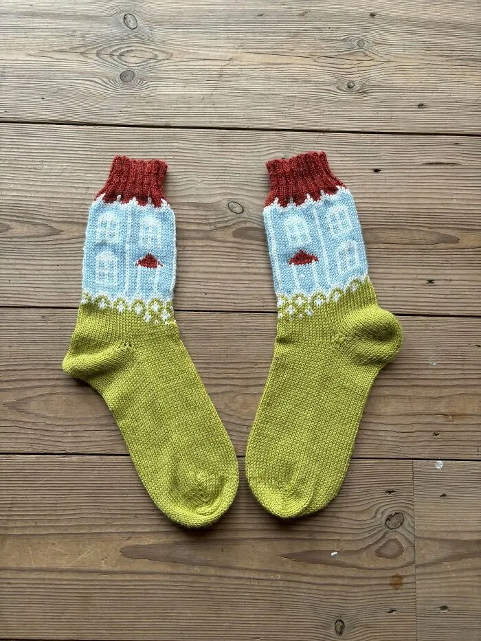 Two yellow and blue socks featuring knitted houses set on wooden floorboards