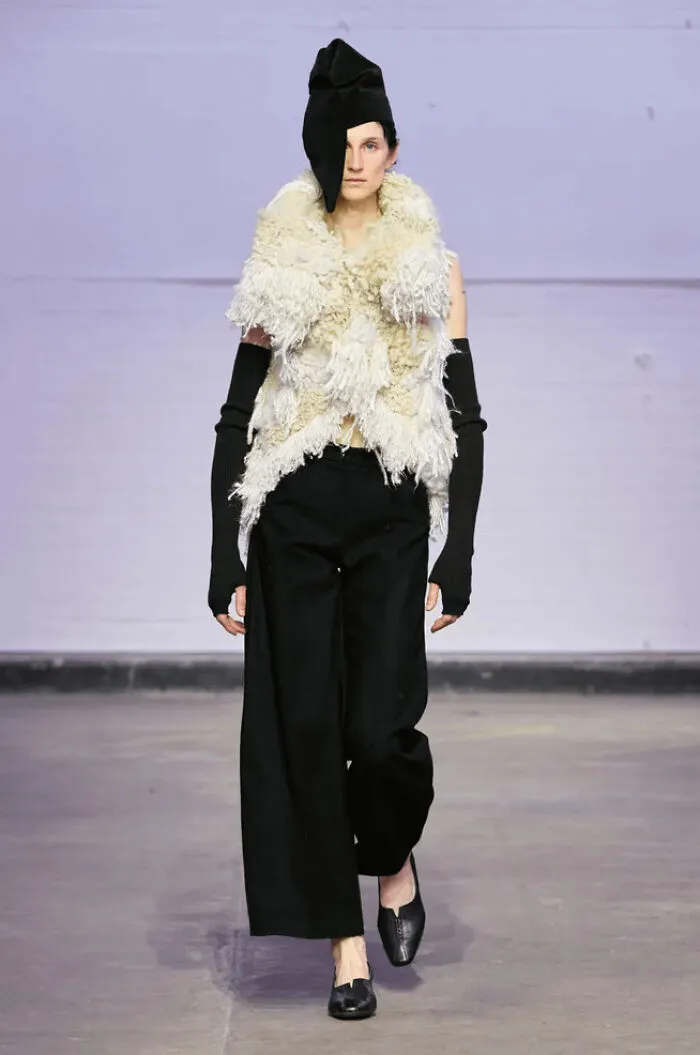 Model wearing a textured cream-colored vest showcase knitting art on a runway