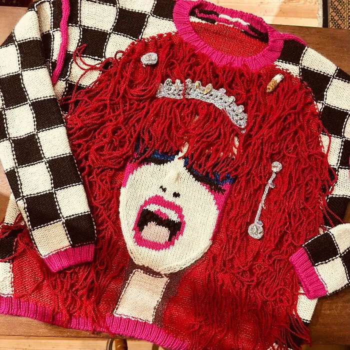 Red sweater depicting a knitted portrait of a face with checkered sleeves