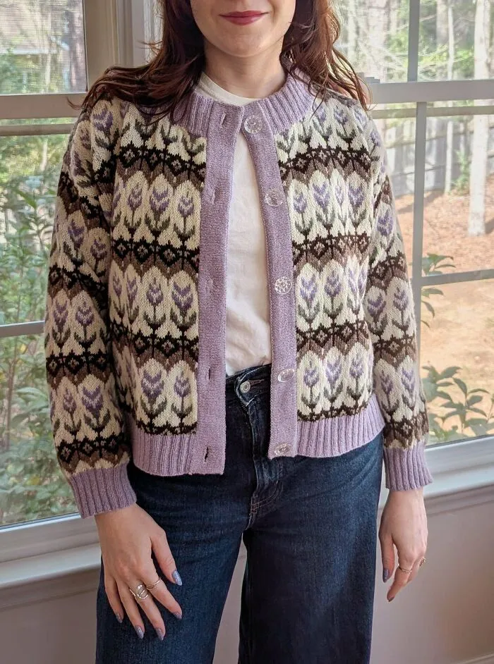 A woman wearing a purple and white knitted cardigan, showing the work of knitting amateurs and pros