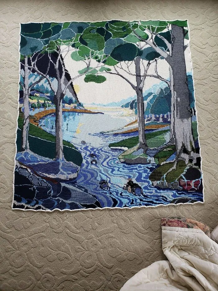 An intricate knitted wall hanging depicting a scenic forest river made by knitting amateurs and pros