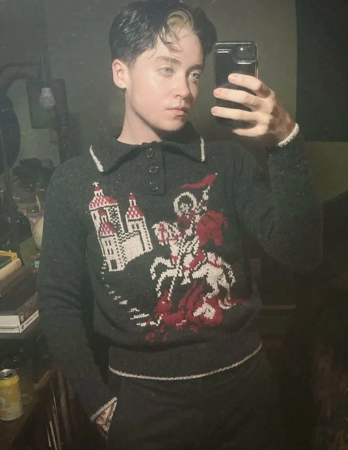 A person taking a selfie wearing a custom knitted sweater with castle and knight design.