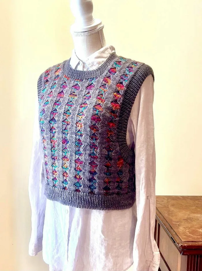A colorful knitted vest displayed on a mannequin over a white shirt, showing complex knitting stitches