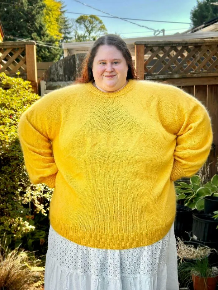 A woman wearing a bright yellow handmade knitted sweater in a garden, demonstrating cozy knitting ideas