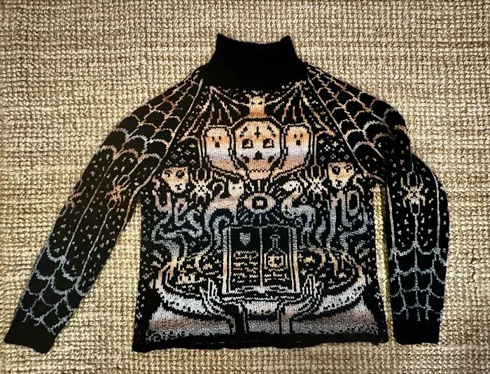 A spooky-themed black knitted sweater with skull and web patterns, illustrating artistic knitting