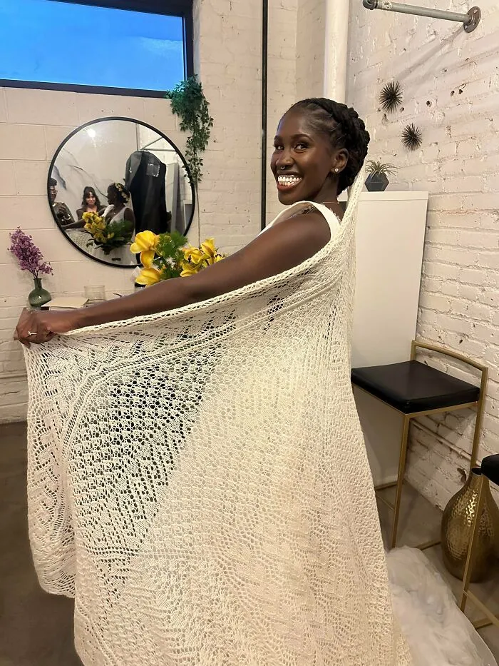 A smiling bride in a stunning, intricate hand-knit wedding dress with a long train.