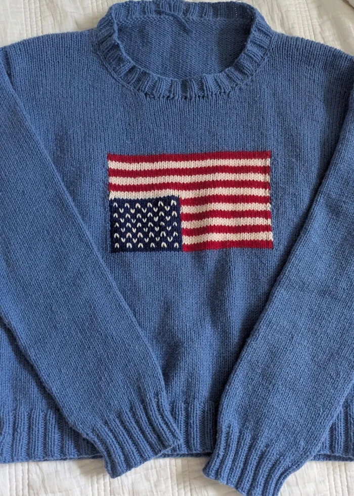 A hand-knitted blue sweater with an American flag pattern showing knitting amateurs skills