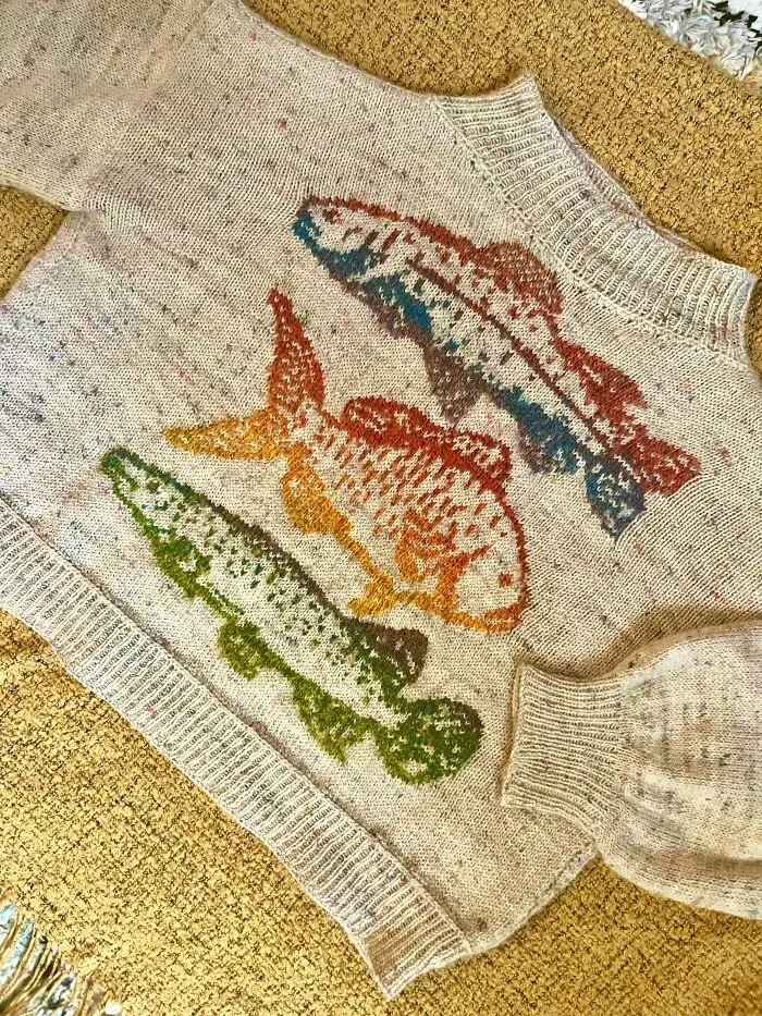 A cozy knitted beige sweater featuring three colorful fish patterns created by knitting pros