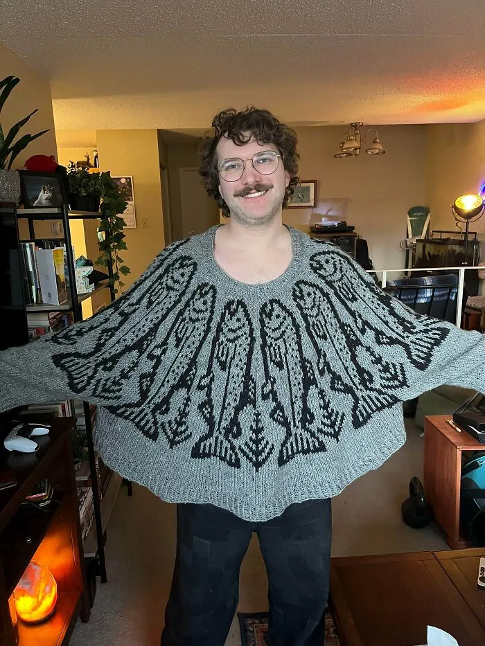 A smiling man wearing a gray fish pattern poncho created by knitting amateurs and pros