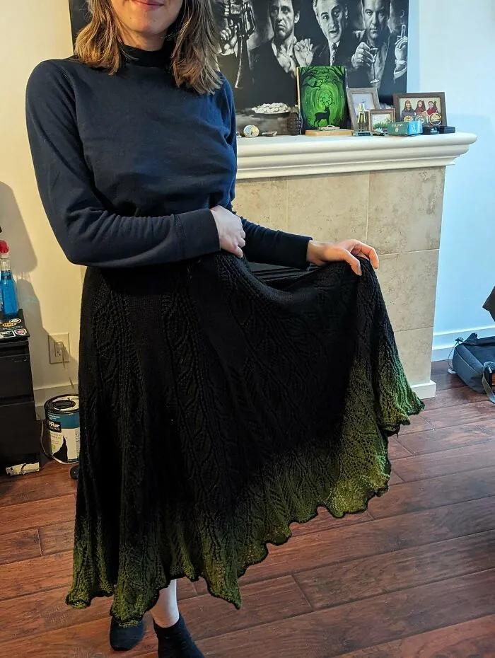 A woman shows off a beautiful knitting design of a black to green gradient skirt.