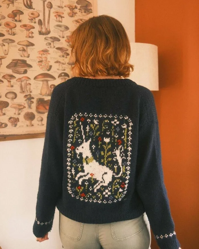 A woman wearing a dark blue sweater with a detailed white unicorn knit pattern on the back.
