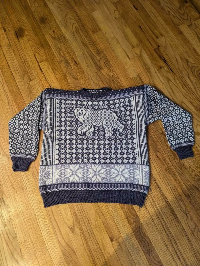 A hand-knitted purple and white wool sweater featuring a walking polar bear pattern, showing expert knitting hobby skills.
