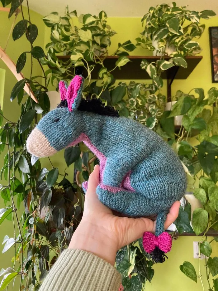 A hand holding a cute, homemade knitted Eeyore plush toy, a delightful outcome of a knitting hobby.