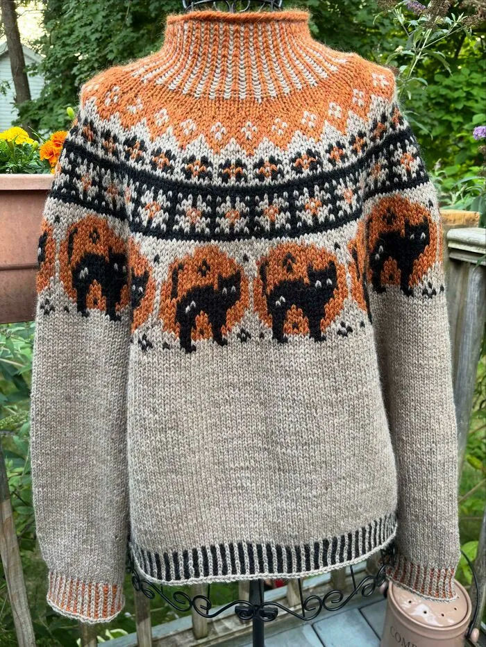 A hand-knitted Halloween sweater with black cats and orange pumpkins, perfect for knitting amateurs and pros.