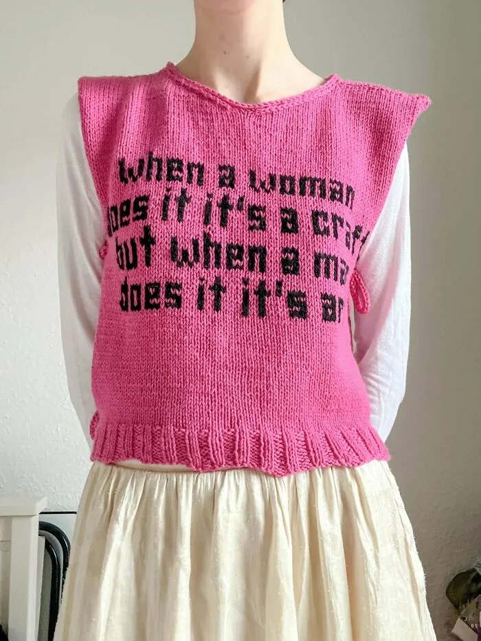 A person wearing a pink knitted vest with black text, illustrating knitting amateurs and pros crafts.