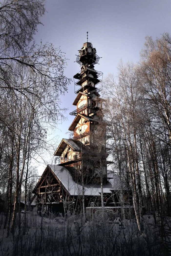 A tall, wooden tower house with bizarre shapes standing in a snowy forest.