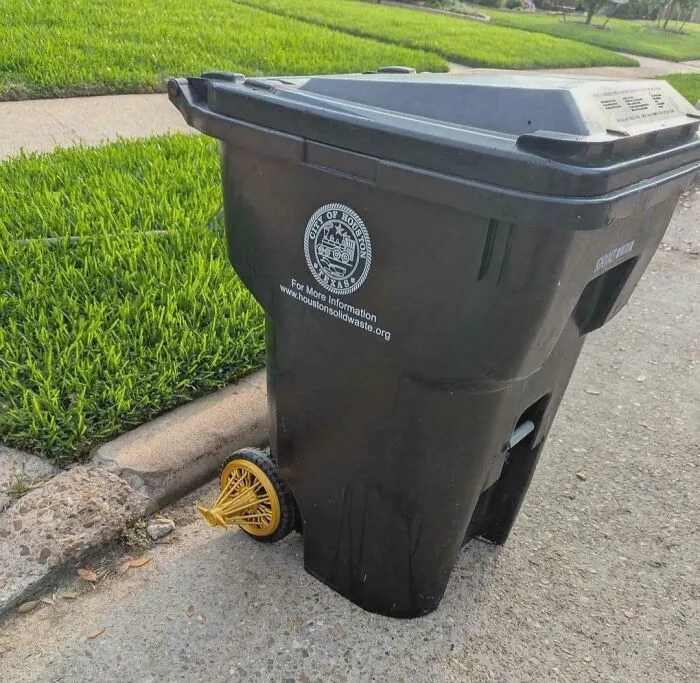 Black plastic trash bin modified with fancy golden wire wheels, showcasing weird and wonderful vehicles.