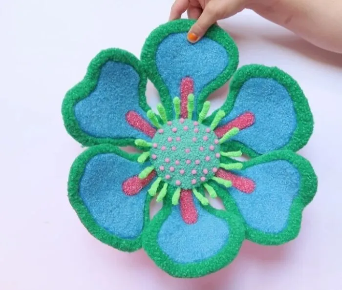 Blue and green tufted flower textile art held by Ina Dyreborg