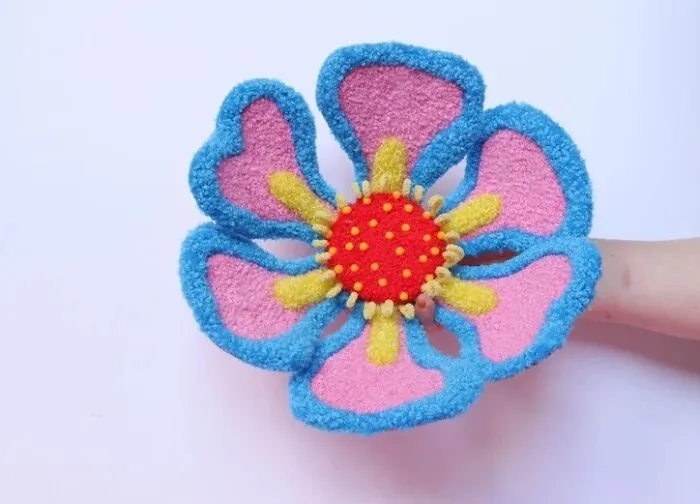 Handcrafted pink and blue tufted flower textile art piece held up by Ina Dyreborg.