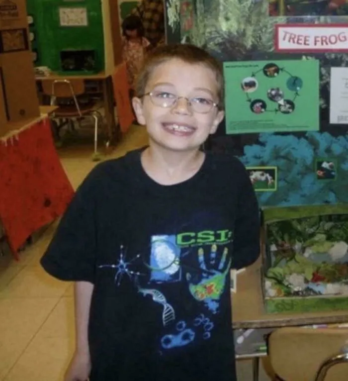 Young boy wearing a black CSI shirt in a classroom setting surrounded by creepy mysteries.