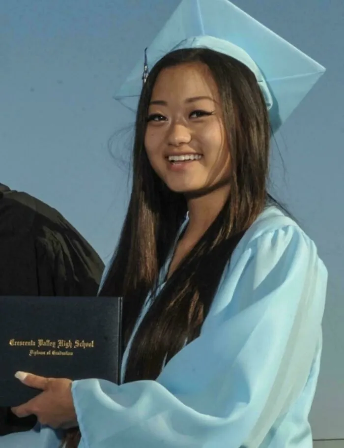 A smiling graduate posing in a light blue cap and gown