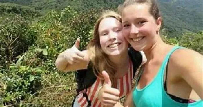 Two young women smiling and giving thumbs up outdoors, involved in creepy mysteries.