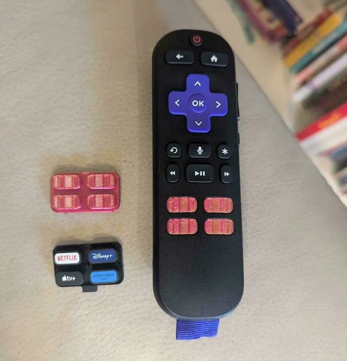 A 3D print custom button blocker inserted into a Roku streaming remote to prevent accidental presses.