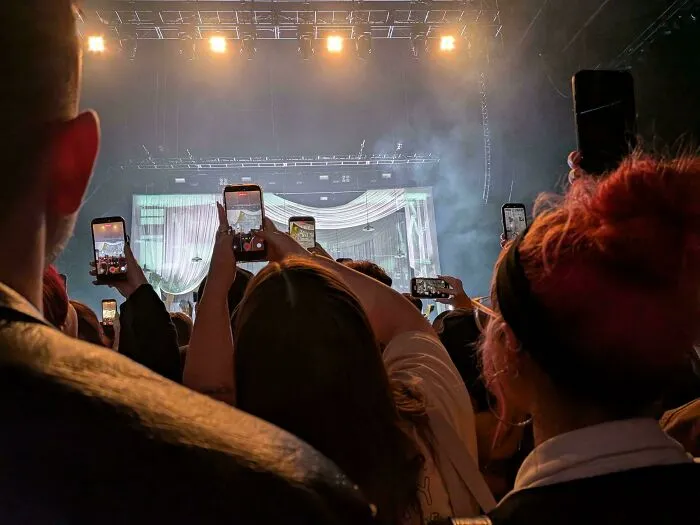 A crowd at a concert holding up smartphones to record, a common scene in modern life in America.