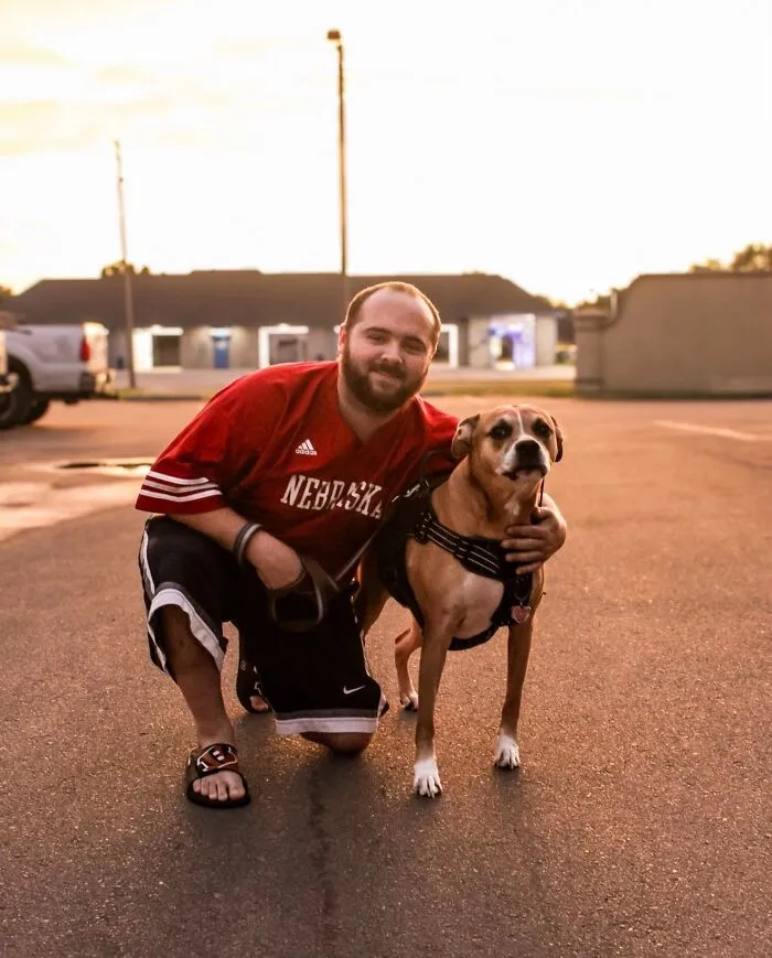 A man in a red jersey kneeling with his dog, sharing life stories with pets.