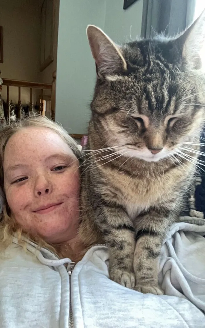 A young woman smiling as her large tabby cat sits on her chest, a TikTok Trend of life stories with pets.
