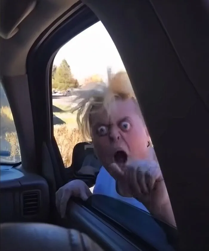 A wild-eyed woman screaming and pointing through a car window, showing unhinged Karen behavior.