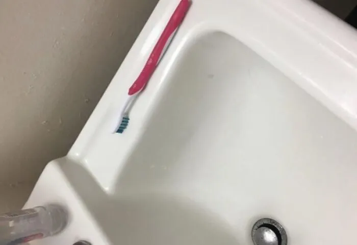 A pink toothbrush placed precariously on the edge of a bathroom sink, illustrating roommate stories of shared spaces.