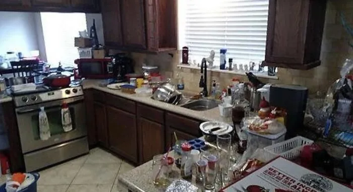 A very messy and cluttered kitchen filled with unwashed dishes and trash on the countertops