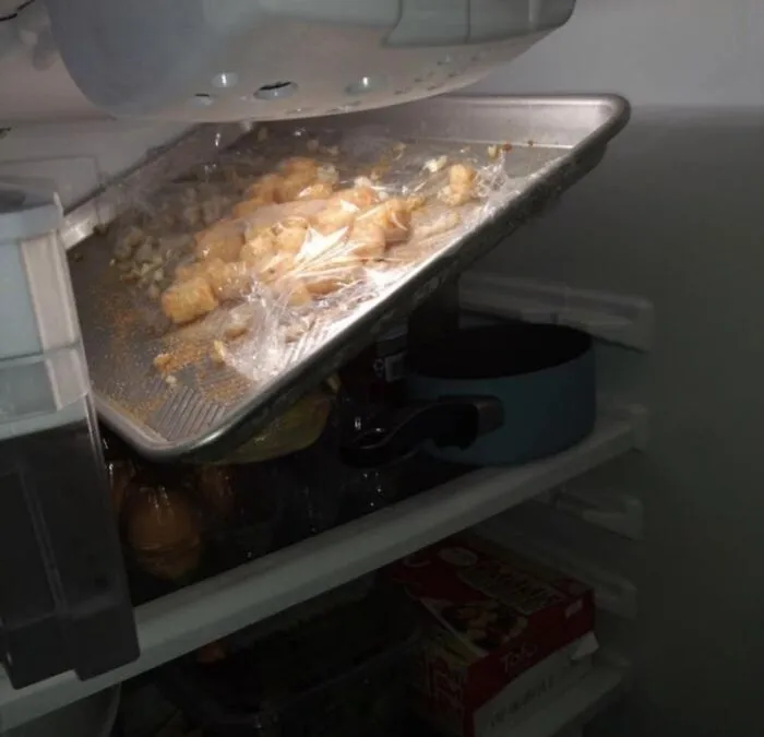 An awkwardly placed baking tray crammed into a refrigerator, showing typical roommate stories of kitchen struggles.
