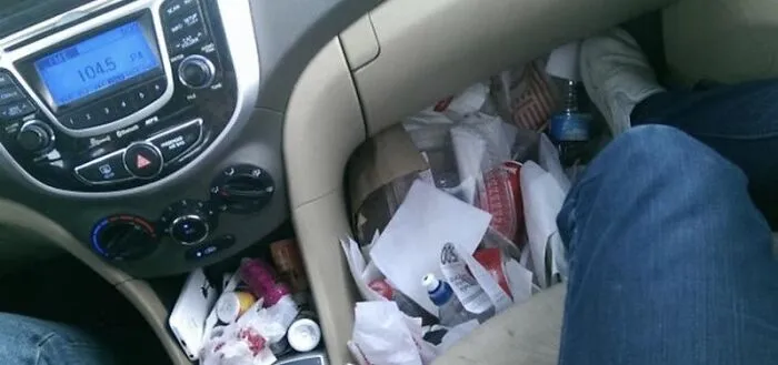 Car floorboard packed with fast food trash and paper, showcasing roommate stories of messy shared vehicles.