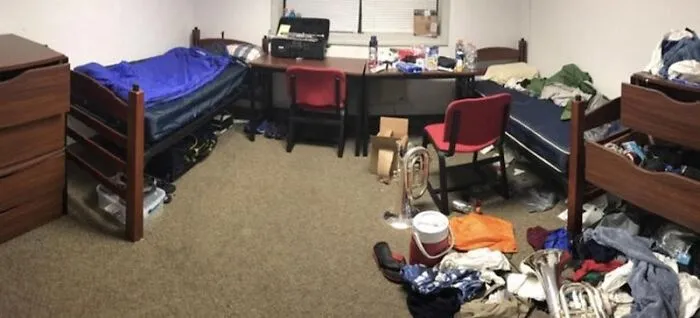 Messy college dorm room with clothes, trash, and musical instruments scattered everywhere