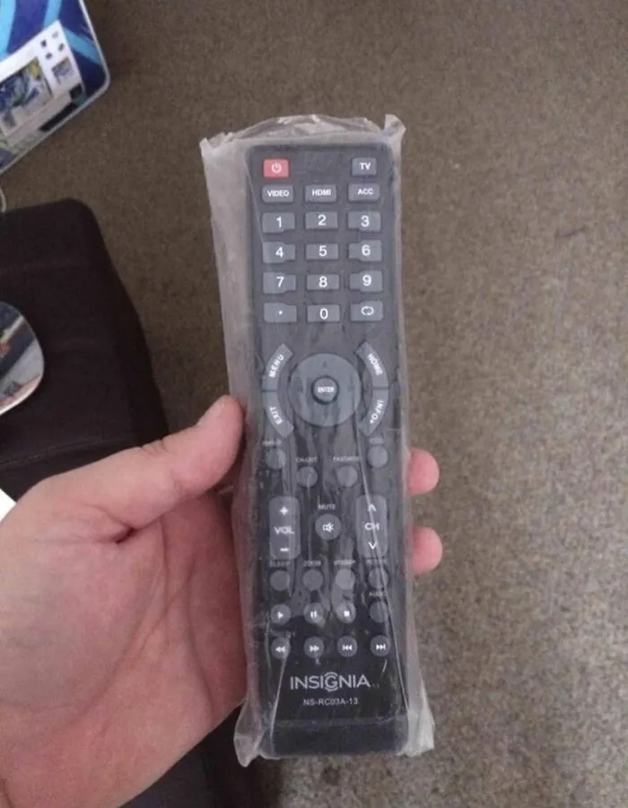 A hand holding a TV remote still sealed in plastic wrapper, illustrating quirky roommate stories.
