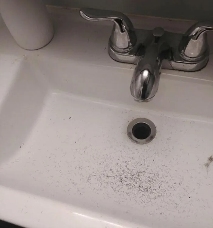 A bathroom sink covered in tiny hair clippings, showcasing annoying roommate stories about shared spaces.