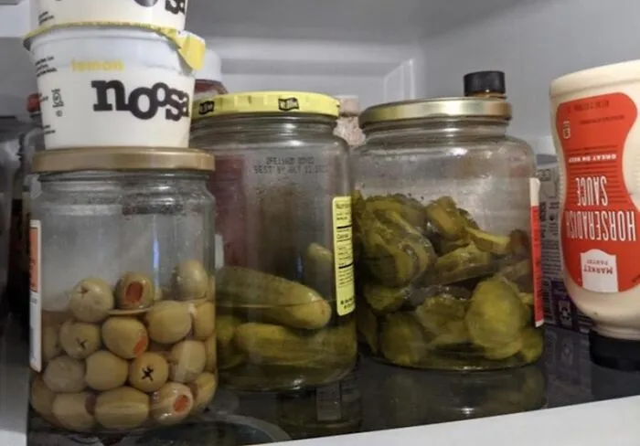 Jars of olives and pickles kept in a messy fridge, a common sight in shared home roommate stories.