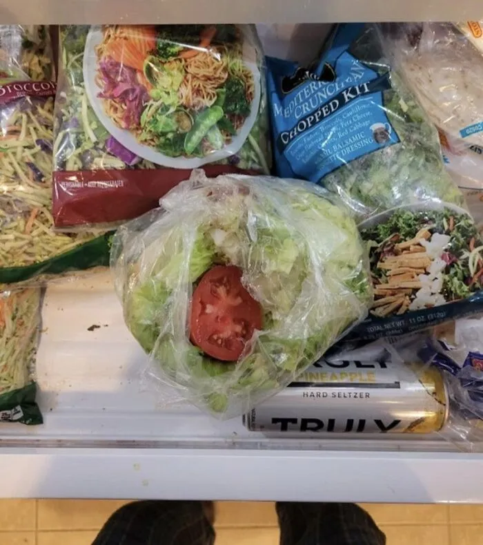 A single tomato slice on a head of lettuce in the fridge, highlighting funny roommate stories.