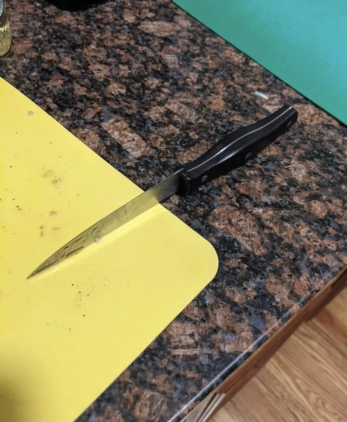 A kitchen knife left precariously on the edge of a yellow cutting board, illustrating frustrating roommate stories.
