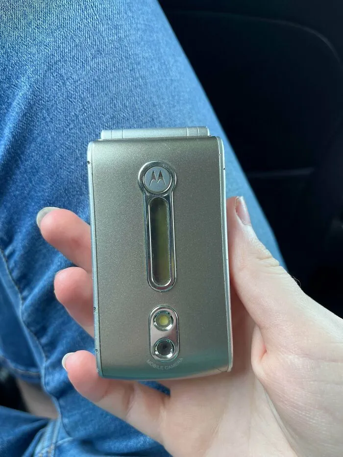A hand holding a classic silver flip phone representing vintage tech finds