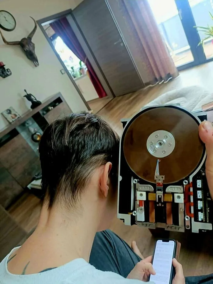 A person comparing a modern smartphone with a giant vintage tech hard drive