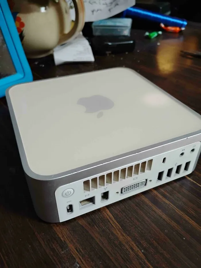 Back view of chunky vintage tech white Apple Mac Mini on wooden table with power port