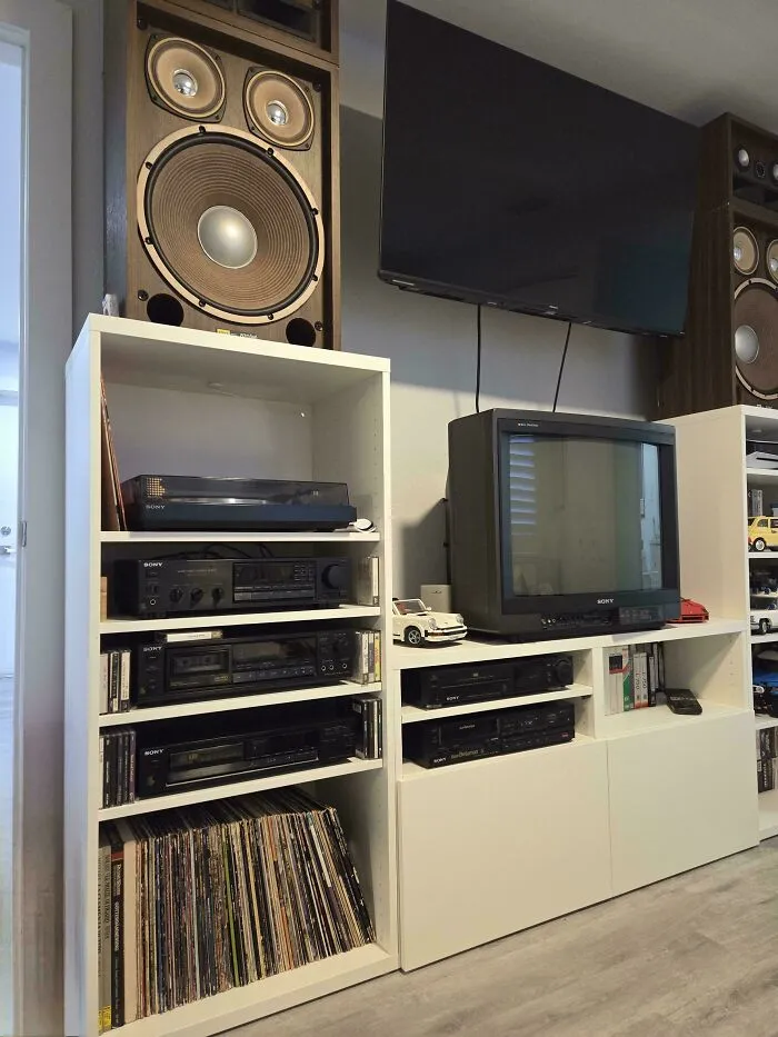An entertainment center filled with vintage tech, including a CRT TV, a record player, and large wooden speakers.