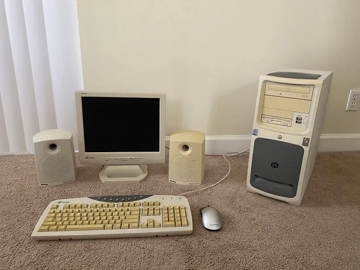 A set of beige chunky electronics including an old computer monitor, keyboard, tower, and speakers on a carpet.