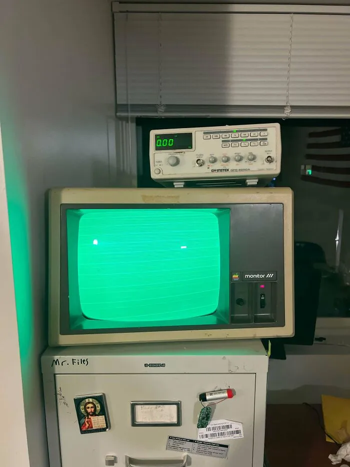 An old Apple Monitor III screen glowing green on top of a filing cabinet representing vintage tech