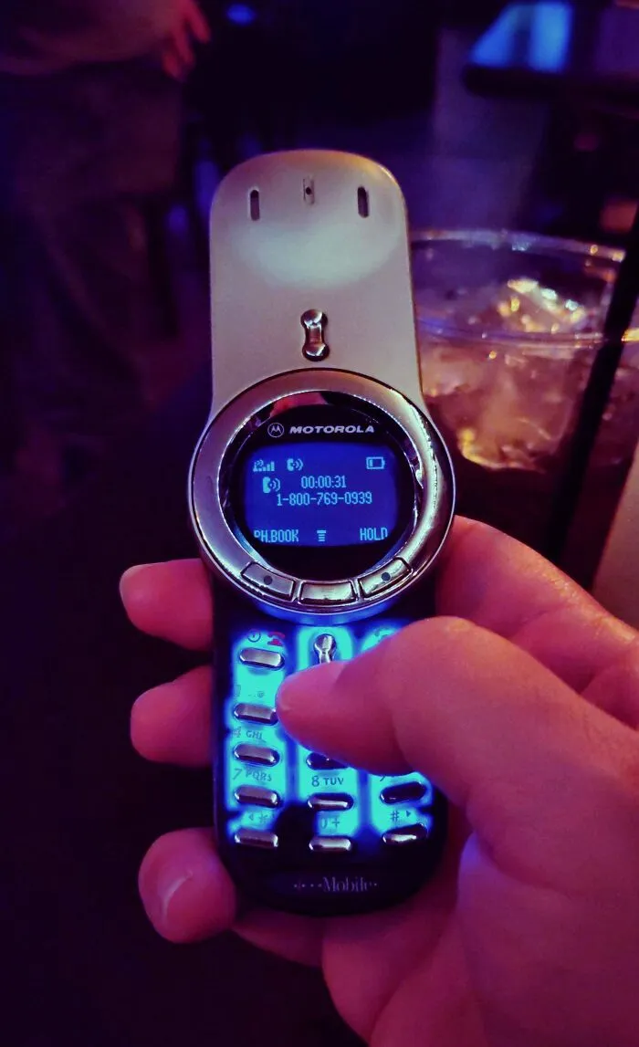 A person holding an old-school Motorola mobile phone featuring classic buttons and a blue backlit screen